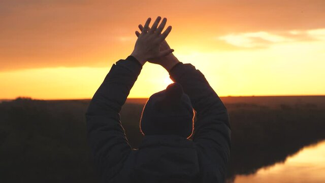 A man waves his hands at sunset asking for help to be found, saved from the danger of getting lost. Male in the glare of the sun is jumping. Man at sunrise on a camping trip or traveling alone
