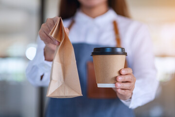 A waitress holding and serving paper cup of coffee and takeaway food in paper bag to customer in a...
