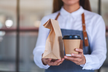 A waitress holding and serving paper cup of coffee and takeaway food in paper bag to customer in a shop