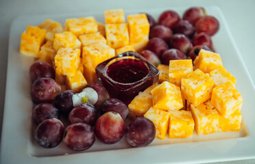 Delicious gourmet appetizer of marble cheese, red grapes and raspberry jam on white plate, close-up. Cold snacks in the restaurant. Catering.