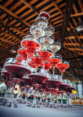 Fototapeta na wymiar High pyramid of wine glasses filled with white and red champagne, view from below. Welcome drink. Organization of an off-site banquet, catering.