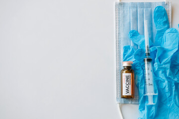 Coronavirus COVID 19 vaccine vial and syringe on medical face mask and blue gloves, white background, copy space. World vaccination concept.