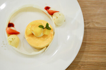 Mango dessert and sour cream parfait dessert topped with slices of mango on a plate decorated with mango puree. Pastel yellow cheesecake colors