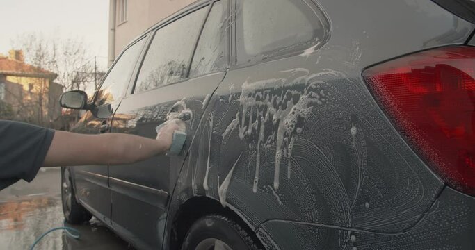 Teenage boy putting soap on a car