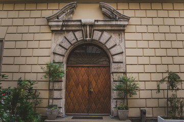 Amazing big old arched two-leaf wooden door with a mosaic window under a semicircular arch of stone. trees and bushes in pots at the entrance to the ancient building with stone wall in Krakow.