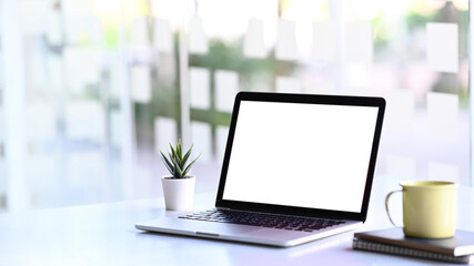 Fototapeta premium Minimal workstation with mock up laptop computer with white screen, plant, coffee cup on white table.
