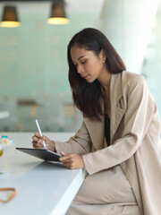 Female working with digital tablet on worktable in glass partition office room