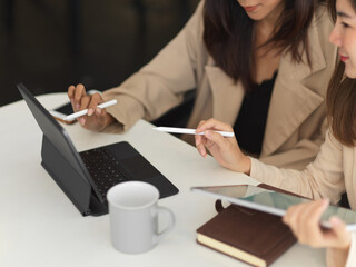 Two businesswomen working together with tablet and supplies in office room