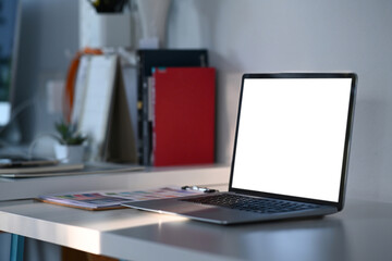 Side view of mock up laptop computer with white screen on graphic designer or designer workspace.