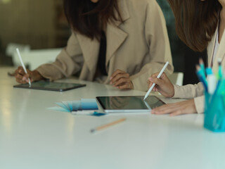 Two female designers working on digital tablet and supplies in meeting room