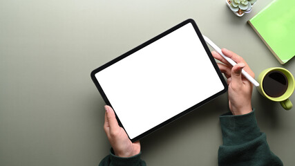 Top view of woman in green sweater holding digital tablet with blank screen and stylus pen on green table.