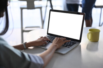 Close up view young woman hands typing on mock up laptop computer with blank screen at her...
