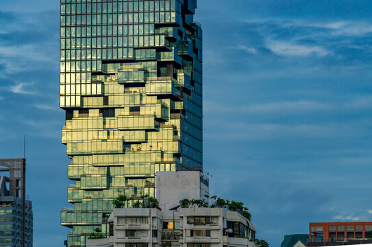 Bangkok, Thailand - Aug 06, 2020 : Beautiful golden morning light on Mahanakorn tower, crop image of the best design part of the glass building. Background of deep blue sky.
