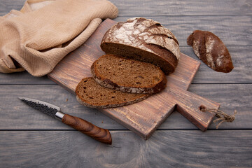 Rye bread round loaf cut into pieces on a wooden board with a knife made of rustic wood.