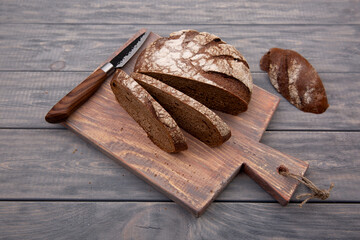 Rye bread round loaf cut into pieces on a wooden board with a knife made of rustic wood. Top view.