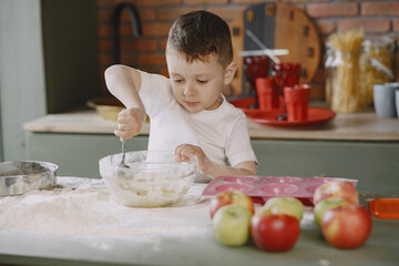 Child in a kitchen. Little boy with a dough. Kid in a white t-shirt.