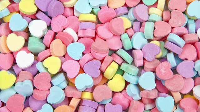 HD video zooming in on background of brightly colored candy hearts for Valentine's Day.
