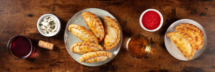 Empanadas with sauces and wine, overhead flat lay panorama on a rustic wooden background