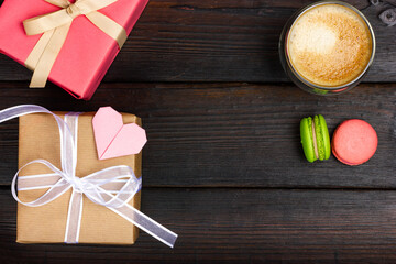 Two gift boxes on a dark wooden table. A glass of latte and two French almond flour macaroon cookies. Festive Flat Lay