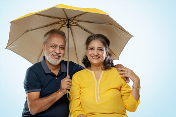 A HAPPY COUPLE SITTING TOGETHER UNDER AN UMBRELLA AND LOOKING AT CAMERA	
