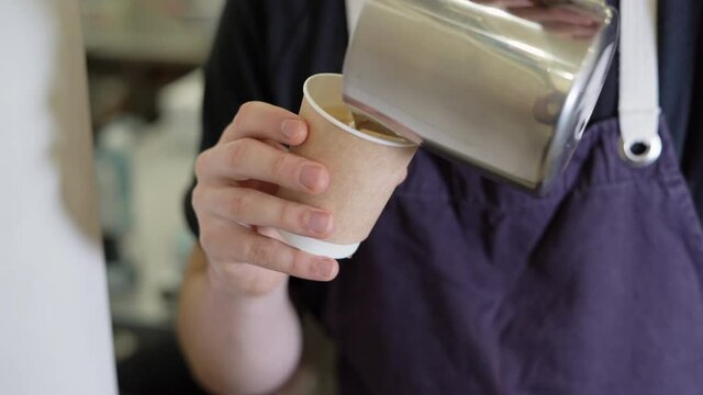 Close up image of male hands pouring steamed milk into disposable paper cup while making latte art coffee. Preparing fresh cappuccino. preparation concept, morning coffee.