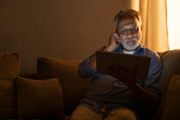 A SENIOR ADULT MAN SITTING AND USING DIGITAL TABLET	