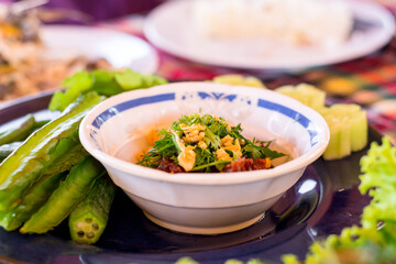 Thai northern chili paste dipping with green coriander chop and deep-fried garlic in white bowl.