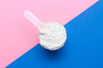 Protein powder in scoop on blue and pink background top view.