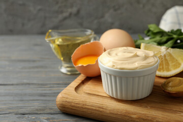 Board with bowl of mayonnaise and ingredients for cooking on wooden background