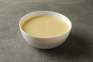 Bowl with condensed milk on gray background