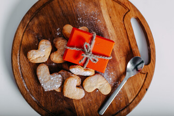 Heart-shaped cookies on round wooden cutting board. Saint Valentine's cookies in shape of heart and red gift box on white background.