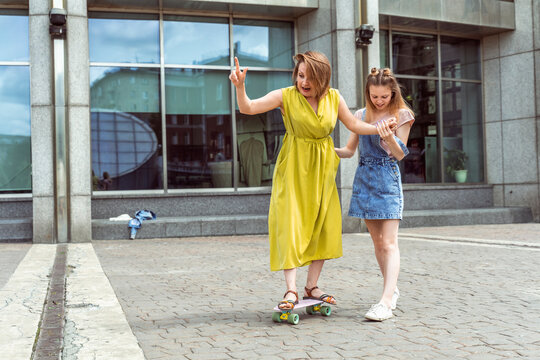 Daughter helping mum on a skateboard. Outdoor lifestyle picture on a sunny summer day.
