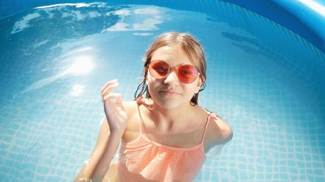 Portrait of cheerful smiling girl relaxing and splashing water in swimming pool on hot summer day. Concept of happy and cheerful summer holidays and vacation