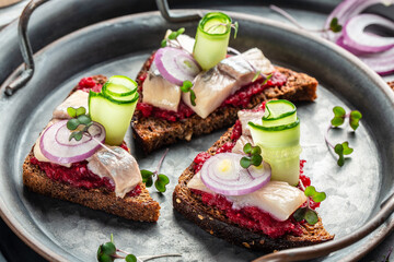 Traditional matie herring with beetroot salad, fresh cucumber and onion rings on rye bread toasts. Scandinavian cuisine