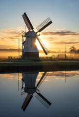 Foggy sunrise at a Dutch windmill reflected in a canal.
