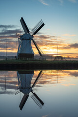 Foggy, winter sunrise at a windmill reflected in a canal.