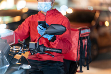 Close up young man working for a food delivery service checking with road motorcycle in the...