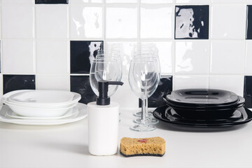 on a white-black tile background, on the table there are clean dishes, plates, glasses and detergents