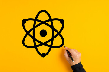 Male hand drawing an atom icon on yellow background. Science and technology