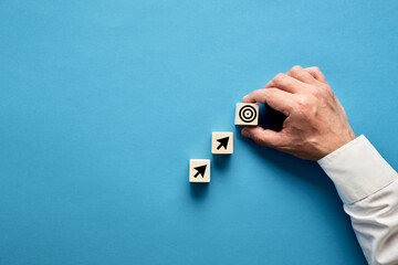 Arrow and target symbols on wooden blocks with a businessman hand placing the target symbol.