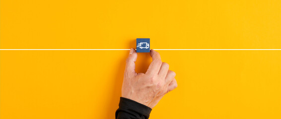 Male hand holds a blue wooden cube with logistics delivery truck icon on yellow background.