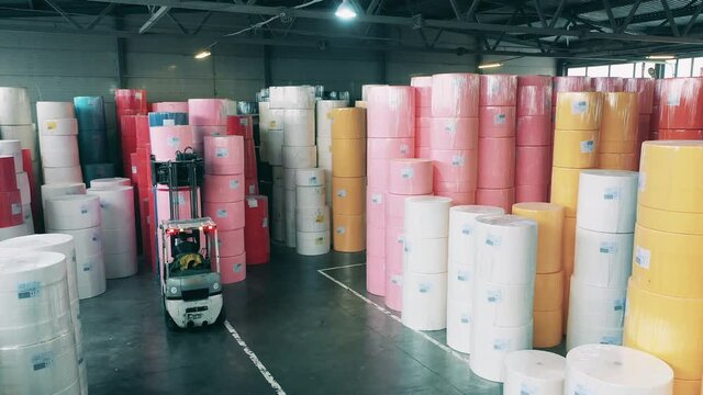 Worker operating a forklift loader to move large paper rolls at a warehouse