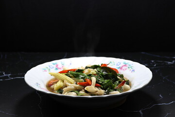 Fried and stirred spicy mushroom with sliced baby corn, chilly, basil and fresh peeled shrimp serving on the plate. 