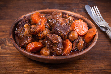 Ready burgundy beef in a clay bowl on a wooden table close up