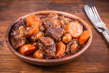 Ready burgundy beef in a clay bowl on a wooden table close up