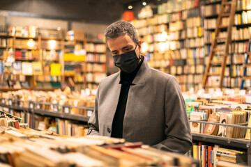 Elegant middle-aged man with mask looking for a book in a classic bookstore Conceptual of...