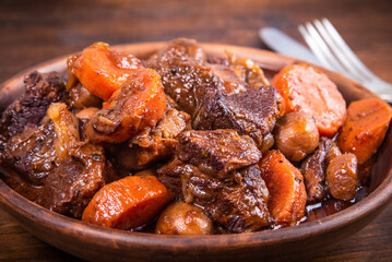 Ready burgundy beef in a clay bowl on a wooden table close up