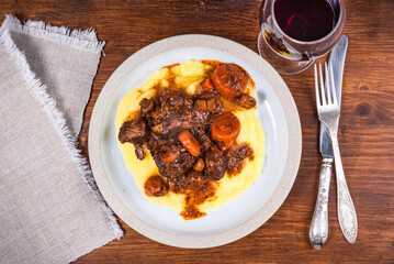 Burgundy beef with mashed potatoes in a plate and a glass of red wine on a wooden table close-up,...