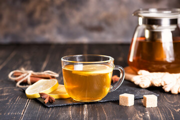 Glass cup of hot ginger tea with lemon on dark wooden table. Sliced lemons on a chopping stone board