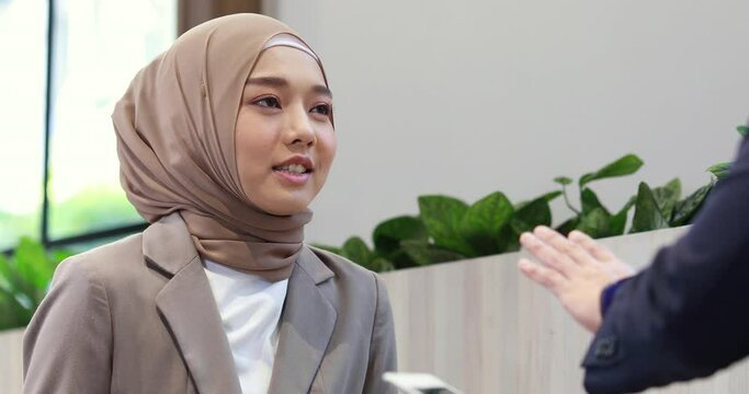 Young business muslim woman and business man colleague walking and discussing outside the office. Woman is holding a coffee and businessman is holding a digital tablet outdoor.